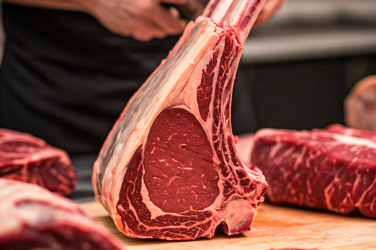 A butcher preparing a tomahawk steak by frenching the long bone.